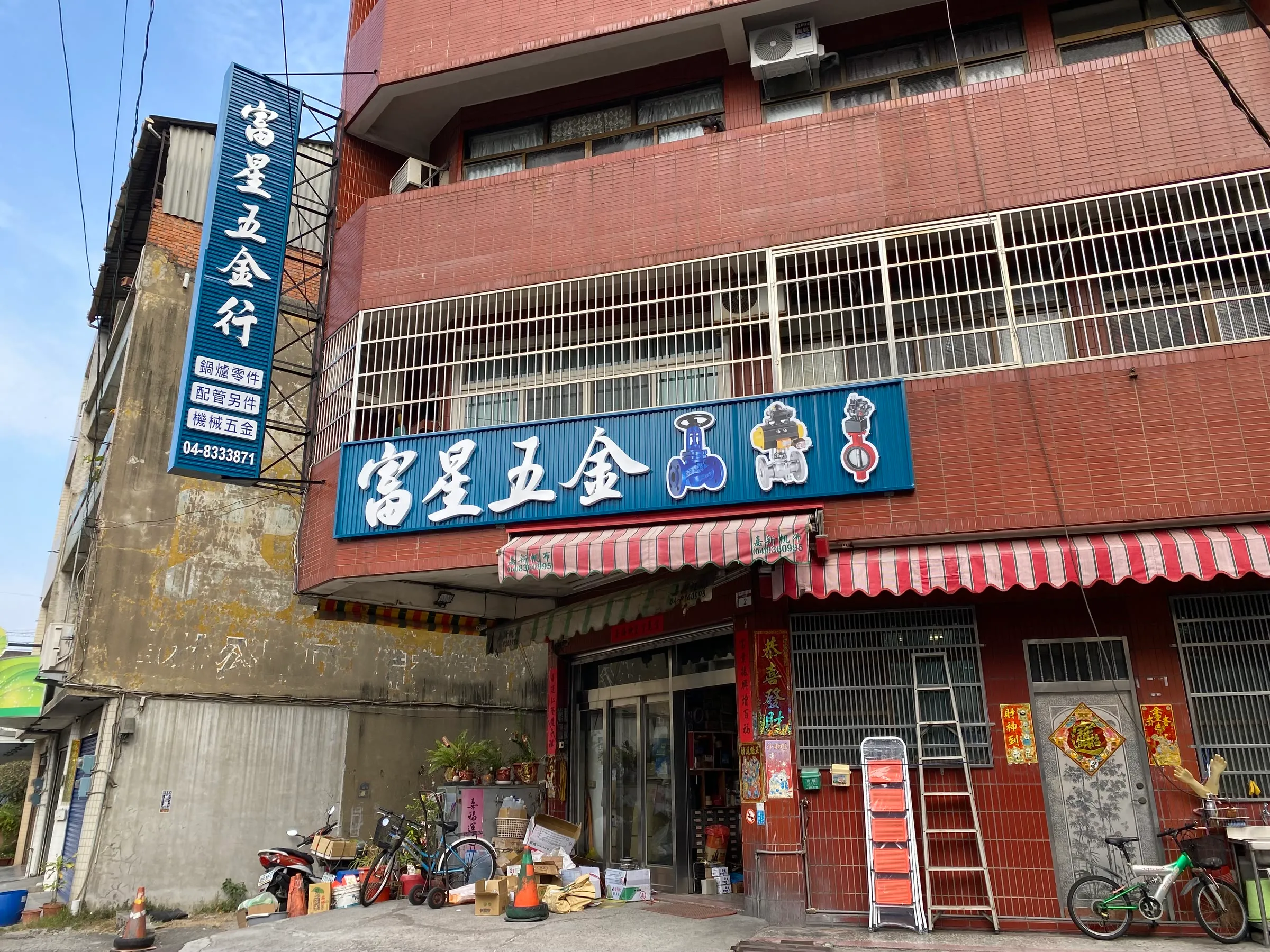 富星五金行店面外觀,藍色招牌寫著富星五金,直式招牌列出鍋爐零件、配管另件、機械五金